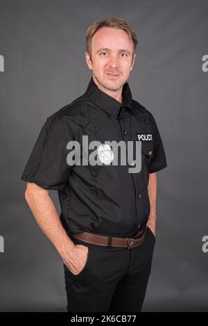 Portrait d'un homme de race blanche portant un costume de police sur fond gris de studio Banque D'Images