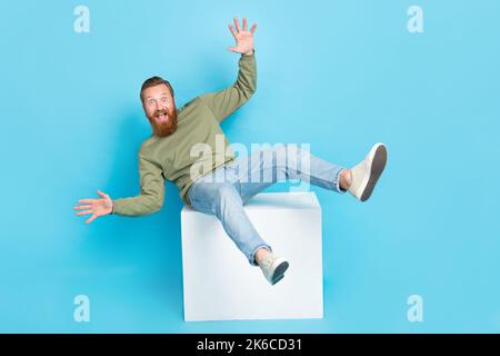 Photo pleine longueur de drôle bonne humeur gars gingembre hairdo kaki long manche tombant de cube blanc isolé sur fond bleu Banque D'Images