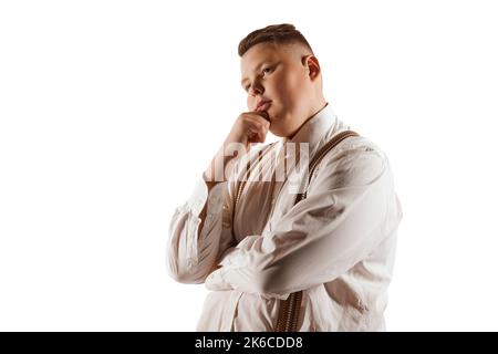 Portrait d'un jeune garçon, modèle en surpoids en chemise blanche et bretelles isolées sur fond blanc de studio. Concept de la jeunesse, des émotions, du visage Banque D'Images