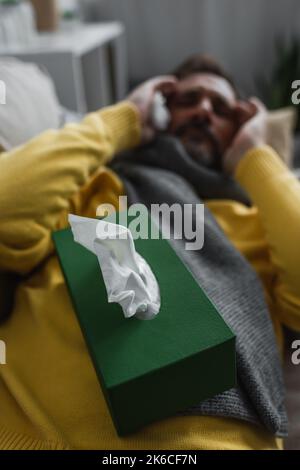 mise au point sélective de l'emballage avec serviettes en papier près de l'homme malade couché et souffrant de maux de tête sur fond flou, image de stock Banque D'Images