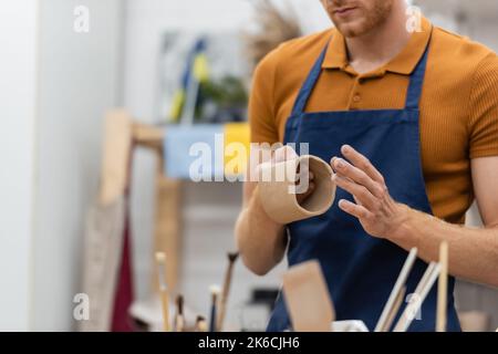 vue rognée de l'homme avec la barbe façonnant la pièce d'argile dans la tasse pendant la classe de poterie, image de stock Banque D'Images