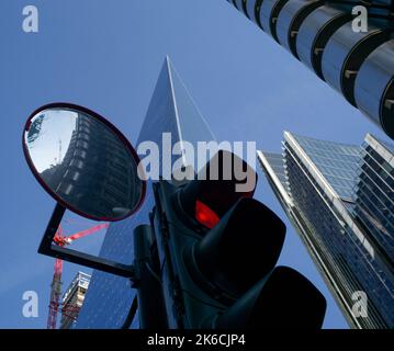 Image conceptuelle d'un gros plan d'un feu rouge avec un miroir de signalisation reflétant le bâtiment Lloyds et les gratte-ciels en arrière-plan. Banque D'Images