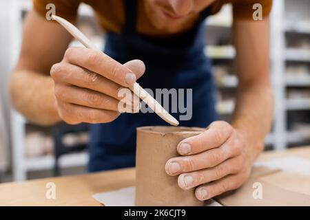 vue rognée de l'homme concentré tenant la couche tout en modélisant la coupe d'argile dans l'atelier de poterie, image de stock Banque D'Images