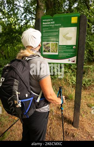 Lady randonnée avec sac à dos et bâtons de marche regardant le panneau sur Beacon Hill le long de la South Downs Way près de Winchester Hampshire Angleterre Banque D'Images