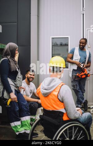 Un jeune ouvrier du bâtiment heureux parlant avec des collègues hommes et femmes pendant la pause sur le site Banque D'Images