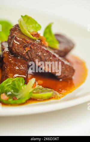 Délicieux joues de veau sauce rouge et verte. Gros plan sur une plaque blanche sur fond blanc Banque D'Images