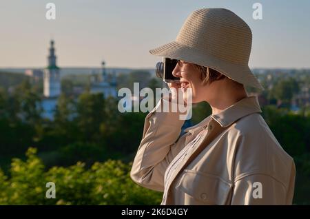 Femme touriste dans un chapeau de paille prend des photos dans la rue avec un appareil photo d'époque Banque D'Images