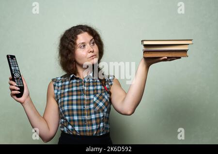 Book vs television. A woman makes a choice between books in one of her hands and a TV remote control in the other Stock Photo