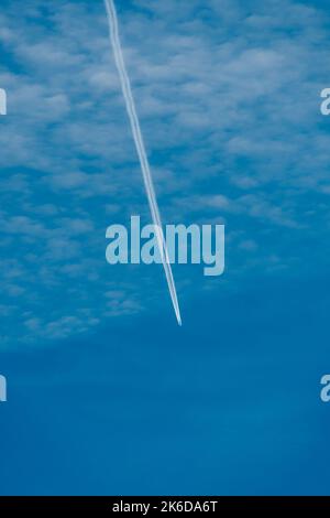 Avion à réaction volant dans un ciel bleu avec des nuages formant de longs contrails blancs. Banque D'Images