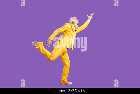 Drôle d'homme âgé en costume jaune chantant et dansant isolé sur fond violet Banque D'Images