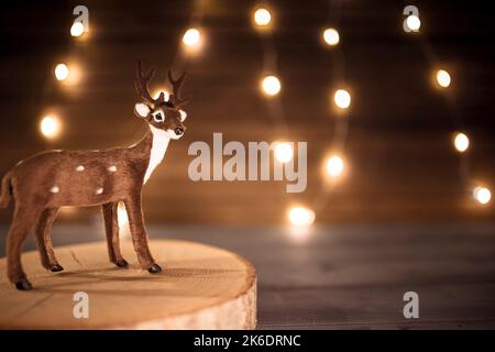 Renne miniature sur plateau en bois, avec guirlande lumineuse en arrière-plan. Papier peint de Noël avec espace de copie. Banque D'Images
