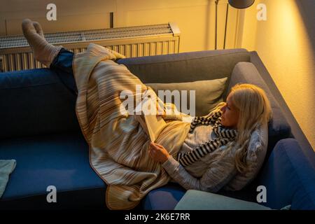 Image symbolique économie d'énergie, hiver froid, crise d'énergie, plat froid, mère et fille couchée, chaudement vêtue sur le canapé, bougie, chauffage sur un Banque D'Images