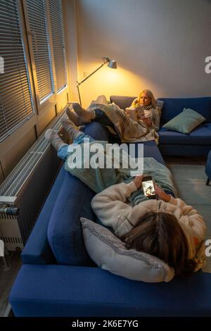 Image symbolique économie d'énergie, hiver froid, crise d'énergie, plat froid, mère et fille couchée, chaudement vêtue sur le canapé, bougie, chauffage sur un Banque D'Images