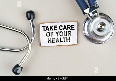 Concept médical. Sur fond gris, un stéthoscope et un panneau en carton avec l'inscription - prenez soin de votre santé Banque D'Images