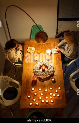 Image symbolique économie d'énergie, hiver froid, crise d'énergie, plat froid, mère et fille vêtues chaudement au dîner, une seule lampe allumée, bougie, chaleur Banque D'Images