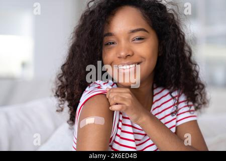 Vaccinée Afro-américaine montrant le bras avec un patch médical de plâtre Plaster sur l'épaule, femelle noire après avoir reçu la dose de vaccin contre le Covid Banque D'Images