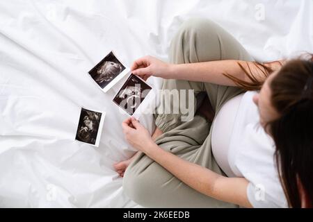 Vue du dessus coupe de la femme enceinte regardant une échographie photo du fœtus debout à la maison, jeune future maman attendant enfant premier bébé, grossesse et Banque D'Images