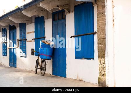 Vieille bicyclette penchée contre un bâtiment blanc et bleu indigo portant des paniers remplis de Kobz, le pain rond marocain typiquement mangé avec du tagine Banque D'Images