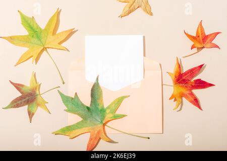 Feuilles et enveloppe automnales avec carte vierge sur fond beige neutre. Concept des vacances d'automne. Vue de dessus, plan d'agencement, maquette. Banque D'Images