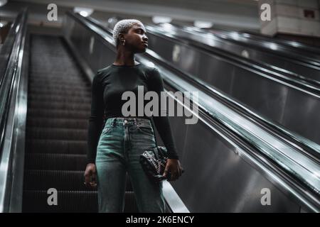 Un portrait d'une jeune fille africaine sur l'escalier roulant descendant vers une station de métro ; une jeune femme noire sur l'escalier en mouvement descendant Banque D'Images