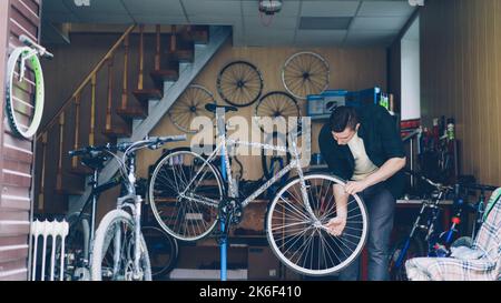 Un mécanicien expérimenté dans les vêtements décontractés est occupé à vérifier le guidon et la roue avant du vélo puis au régler et au fixer avec des outils. Les cycles de réparation et le concept de personnes. Banque D'Images