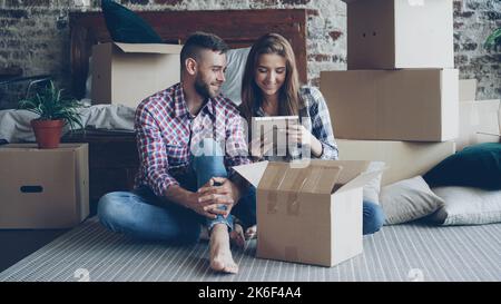 Heureux couple est de déballer les choses après la réinstallation ouverture boîte de carton et regardant des photos parler et rire ensemble. Passage à un nouveau concept de maison et de relation. Banque D'Images