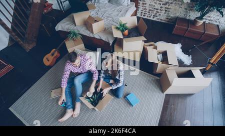Vue de dessus de jeune couple heureux de déballer des choses, d'ouvrir boîte de carton, de prendre des choses et de parler après avoir changé d'appartement. Concept de relation et de relocalisation. Banque D'Images