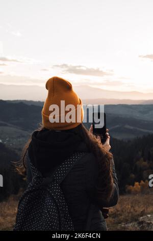 La jeune femme en bonnet orange de derrière prend une photo de la vue sur les montagnes Banque D'Images