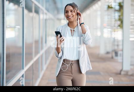 Écouteurs, téléphone et femme d'affaires en ville, diffusion audio, podcast ou musique. Souriez, détendez-vous et une femme de l'Inde marchant, en pause ou 5g application mobile Banque D'Images