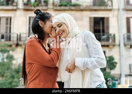 Femme chuchotant un secret à son ami à l'extérieur dans la rue. Banque D'Images