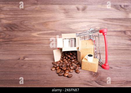 Chariot de poussée de jouet renversé rempli de cartons contenant des grains de café torréfiés et des gobelets en papier isolés sur un fond en bois sombre. Banque D'Images