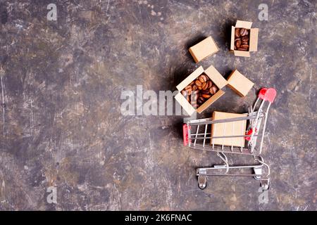 Chariot de poussée miniature renversé et lot de petites boîtes en carton avec grains de café torréfiés isolés sur un fond sombre coloré avec espace de copie. Banque D'Images