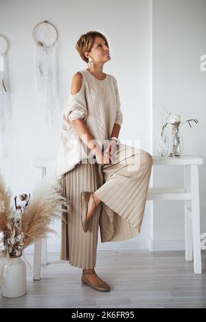 Belle femme, designer d'intérieur pensant comment décorer une nouvelle maison. Elle porte un chandail et un pantalon beige. Banque D'Images