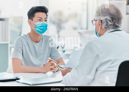 Nous prenons la sécurité au sérieux dans la clinique. un jeune homme portant un masque facial et assis avec son médecin pendant sa consultation à la clinique. Banque D'Images