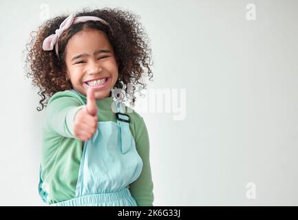 Ça m'a fait un pouce. une adorable petite fille debout seule et montrant un pouce vers le haut sur un fond gris. Banque D'Images