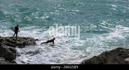 Image panoramique d'un surfeur se lançant dans la mer depuis les rochers de Pentire point East à Newquay, en Cornouailles, au Royaume-Uni. Banque D'Images