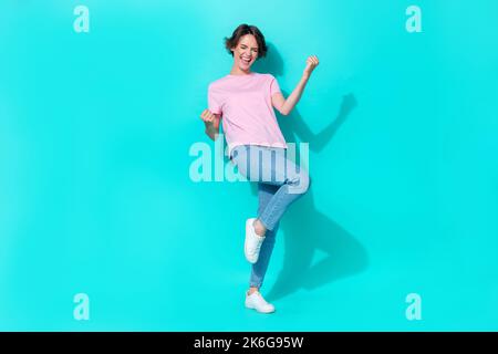 Photo pleine grandeur de jolie petite fille rose t-shirt jeans blanc baskets hurlez oui lève les poings vers le haut bonne humeur isolé sur fond de couleur sarcelle Banque D'Images