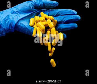 Pilules médicales sur un fond noir isolé avec réflexion abandonnée de la main Banque D'Images