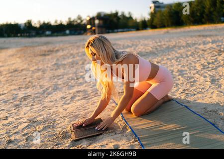 Portrait d'une jeune femme blonde tenant le tableau Sadhu avec les ongles dans les mains et touchant les ongles pointus avec la paume sur la plage de sable à l'été matin ensoleillé. Banque D'Images