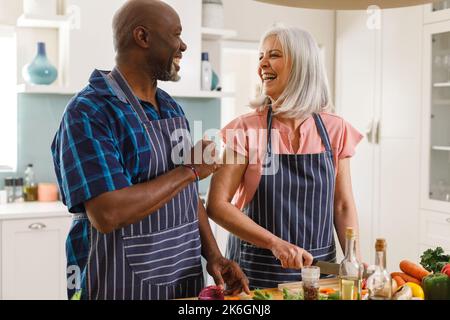 Joyeux couple senior divers portant des tabliers et cuisinant dans la cuisine Banque D'Images