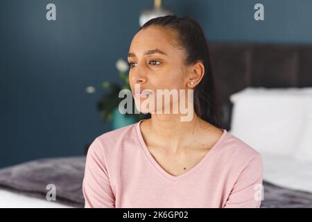 Femme biraciale attentionnés assise sur le lit et donnant sur la maison Banque D'Images