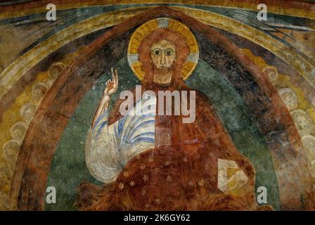 Christ en fresque majesté, peint au début de 1100s, dans la cathédrale Saint-Cyr-et-Sainte-Julitte à Nevers, Bourgogne-Franche-Comté, France. Jésus aux yeux noirs, épais cheveux rouges encadrés par un halo doré, lève sa main droite dans un geste de bénédiction. Banque D'Images