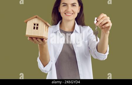 Femme dans une chemise blanche tient une maquette en bois d'une maison et les clés de la maison. Banque D'Images