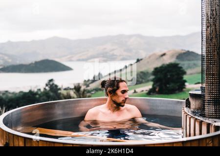 homme caucasien avec de longs cheveux recueillis avec une barbe sérieux détendu et calme à l'intérieur d'un petit jacuzzi rond en bois et de l'eau chaude au milieu de la Banque D'Images