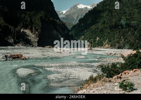 riverbed d'eau transparente formée par la fonte de la glace entre les montagnes boisées et enneigées faisant son chemin à travers les pierres dans un endroit solitaire et calme Banque D'Images