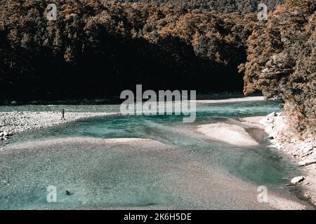 jeune caucasien sur la rive d'une rivière calme et pierreuse avec des eaux transparentes dans un environnement très lumineux parmi la végétation et les arbres de Banque D'Images