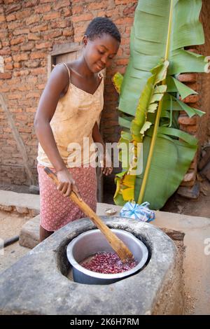 Les cuisinières à faible consommation de carburant, comme celle que l'on voit ici dans le district de Kasese, en Ouganda, utilisent moins de bois de chauffage et sont plus saines parce qu'elles produisent moins de fumée. Ici, une fille agite un pot de haricots sur le poêle. Banque D'Images