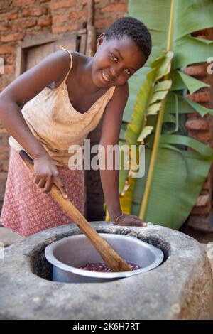 Les cuisinières à faible consommation de carburant, comme celle que l'on voit ici dans le district de Kasese, en Ouganda, utilisent moins de bois de chauffage et sont plus saines parce qu'elles produisent moins de fumée. Ici, une fille agite un pot de haricots sur le poêle. Banque D'Images