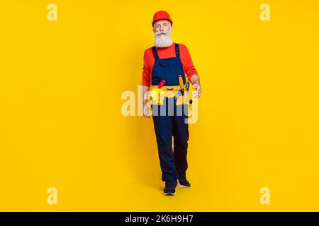 Photo pleine longueur de l'âge frais confiant homme porter ensemble uniforme rouge casque de marche vide espace isolé couleur jaune arrière-plan Banque D'Images