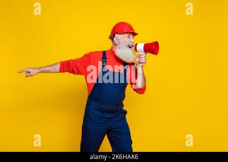 Photo de la colère sérieux vieux gars habillé uniforme général rouge hardhat hurlant toa pointant le doigt vide espace isolé couleur jaune arrière-plan Banque D'Images